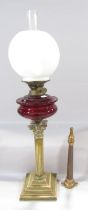 A Victorian brass Corinthian column oil lamp, with a bright red font and opaque white shade,