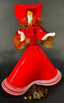 A Murano glass lady wearing a flared red A line dress with gold ruffled sleeves and flamboyant