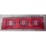 Oriental carpet runner, with three central medallions, on a deep red ground, 274 x 78 cm