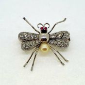 White metal fly, a body of metal and pearl with open work diamond set wings and two ruby eyes.