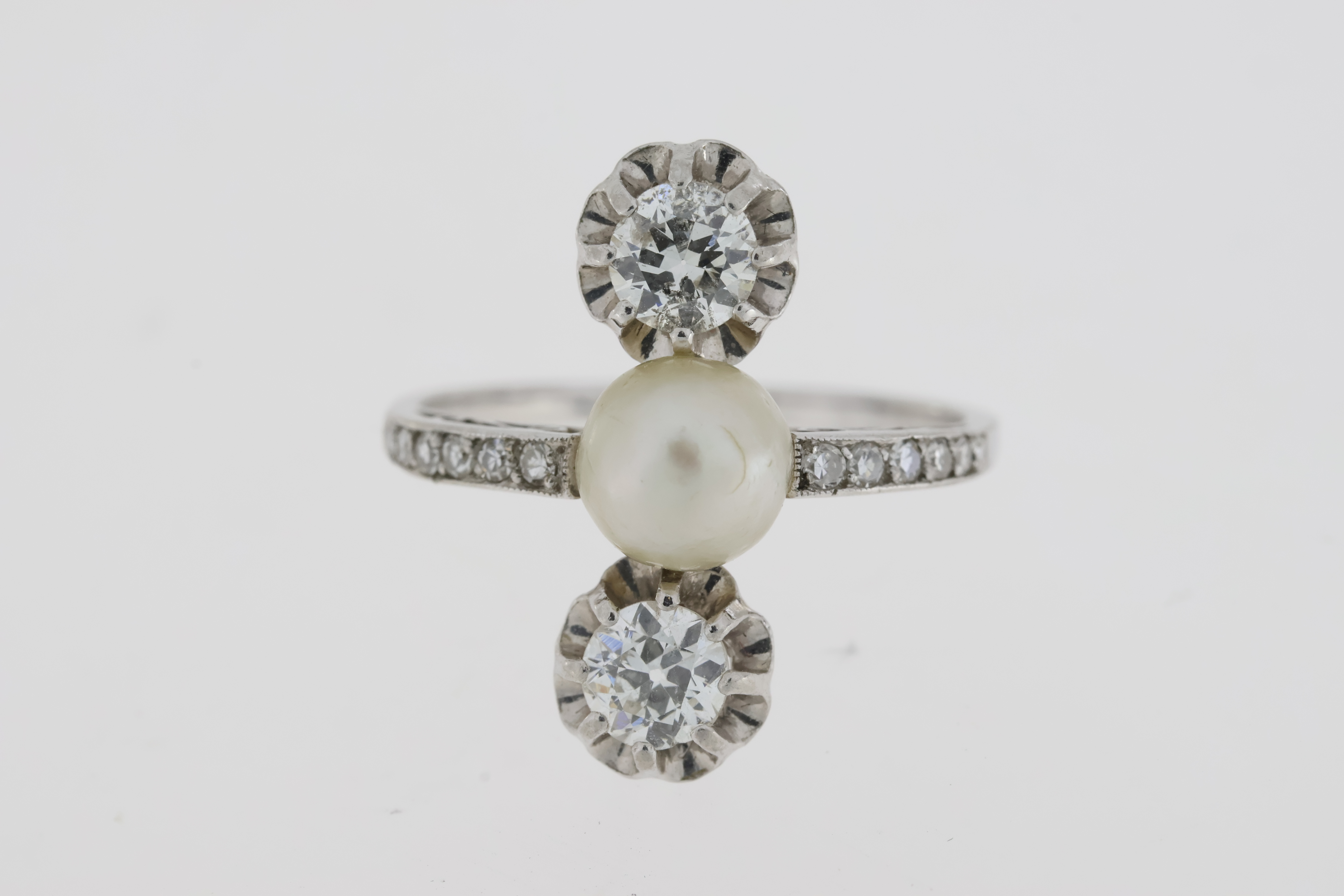 An art deco platinum trilogy ring comprising anatural pearl set between two old cut diamonds.