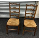 A pair of ladder back chairs with straw sits