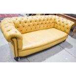 A modern Chesterfield settee upholstered in mustard coloured leather, raised on turned wooden