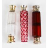 Three Victorian scent bottles; one cut glass with cranberry overlay, the white metal top enclosing a