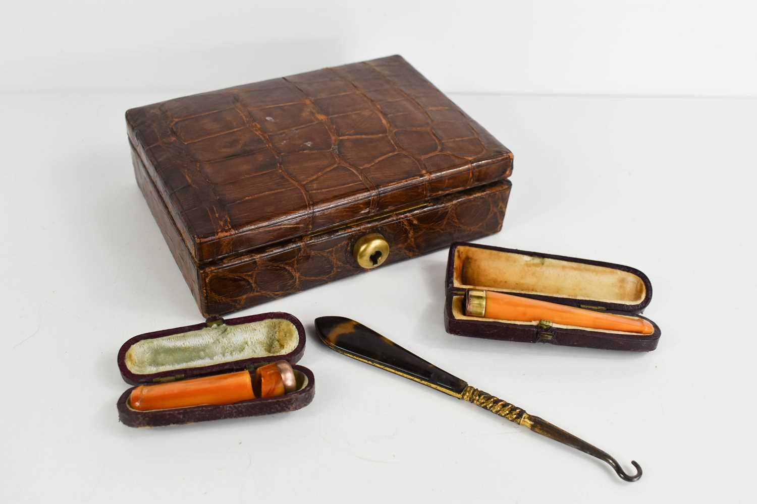 An early 20th century crocodile skin jewellery box together with two amber cheroot holders, one with