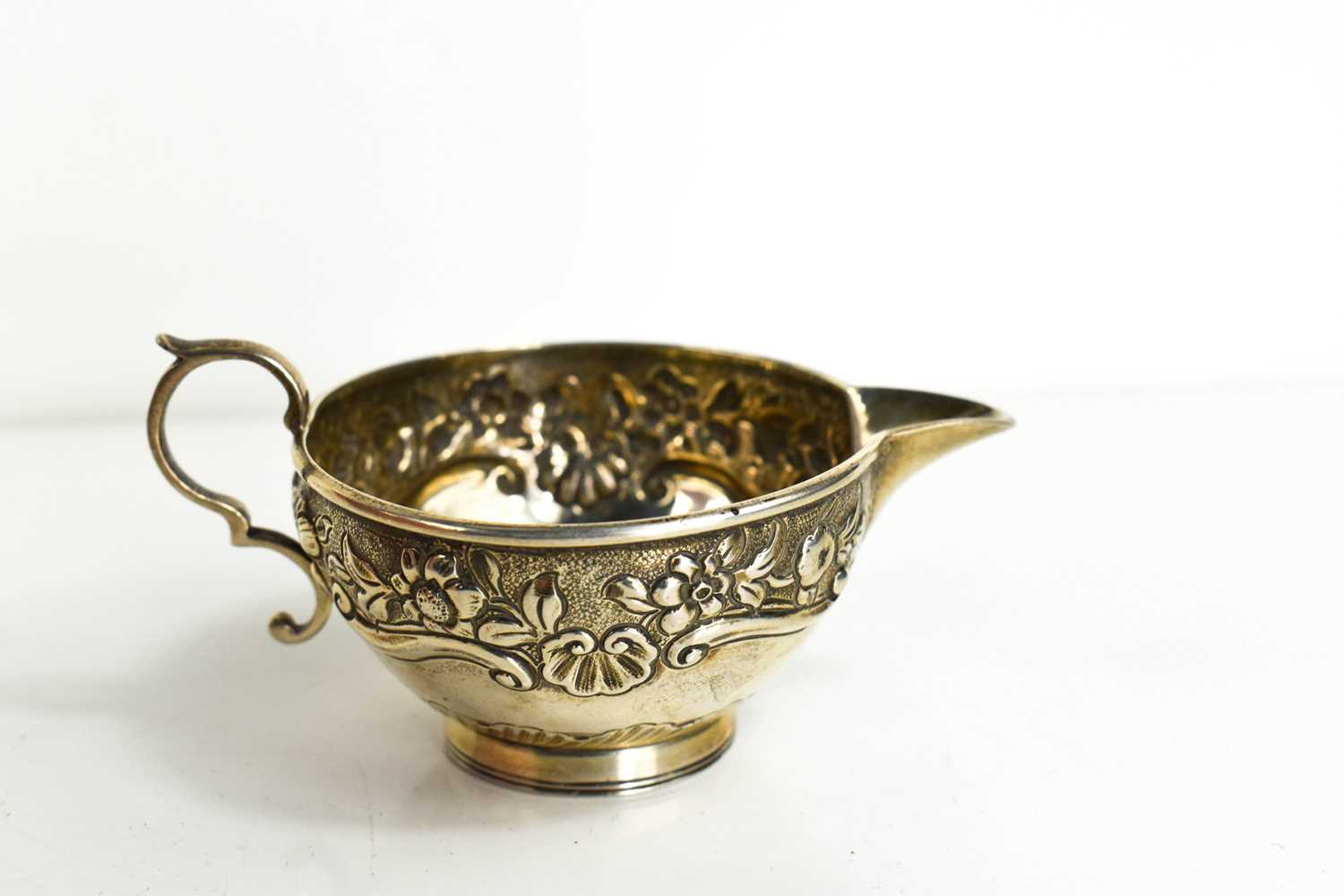 A Victorian small silver cream jug, of cup form, chased with flowers and scallop shells, with curled