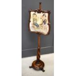 A Victorian mahogany pole screen, the cartouche form screen having a needlework panel depicting card
