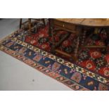 A Middle Eastern rug with red central ground with lozenge stylised floral motifs with blue and cream