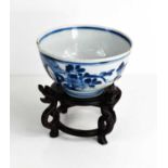 A 19th century Chinese blue and white bowl decorated with flowers, and raised on a wooden carved