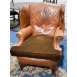 A 1930s tan leather wingback armchair with brass studwork, raised on short cabriole legs.The leather