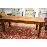 A large pine kitchen table with planked top with two drawers and raised on boldly turned legs,