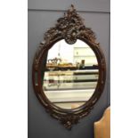 A large and impressive oval mirror, with carved rococo darkwood frame, 141 by 82cm.