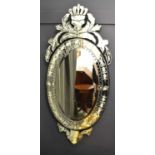 A large oval mirror in the Venetian style, with coronet pediment above, etched decorative border and