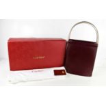 A Cartier Handbag of concertina form in burgundy leather with three arched tri-gold coloured metal