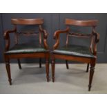 A pair of Victorian mahogany armchairs, with green leatherette seats, the scroll arms raised above