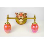 A kitsch wall sconce in the form of a tiger holding the lights in its jaw, with two pink acorn