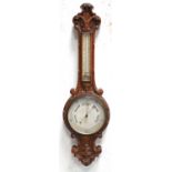 A late Victorian carved oak aneroid banjo barometer with a mercury thermometer.