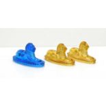 A pair of Victorian amber glass lions, in recumbent position and another similar in cobalt blue.