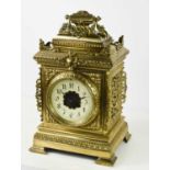 A 1920s brass mantle clock, cast with a garland surmount, face mask & shield applique, and having an