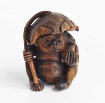 A Japanese carved wooden netsuke of a monkey sheltering under a leaf, with glass eyes and signed