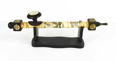 A bone opium pipe with inscribed and coloured decoration on stand.