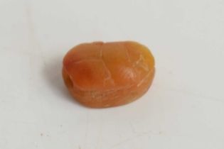 A tiny Egyptian scarab beetle bead carved from an amber coloured stone, the base having a carved