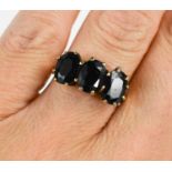 A 9ct gold and dark sapphire three stone ring, each of the oval cut almost black sapphires of