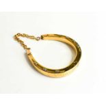 A gold horse shoe form bangle, engraved 'Wear it for Good Luck', each of the 'nails' in white