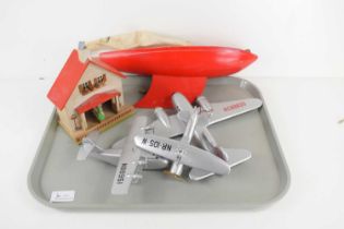 A small wooden pond yacht with red hull, a group of three model aeroplanes and a weather house. [