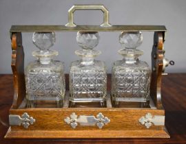 A vintage oak tantalus containing three cut glass decanters with their stoppers.