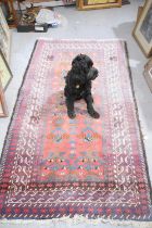 A Middle eastern red ground rug with stylised geometric borders, 205cm by 107cm