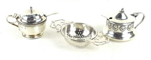 A silver tea strainer together with two silver mustard pots, one embossed with tulips, with glass