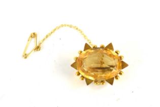 A gold (unmarked) and citrine brooch, the oval cut citrine within a border of triangular and ball