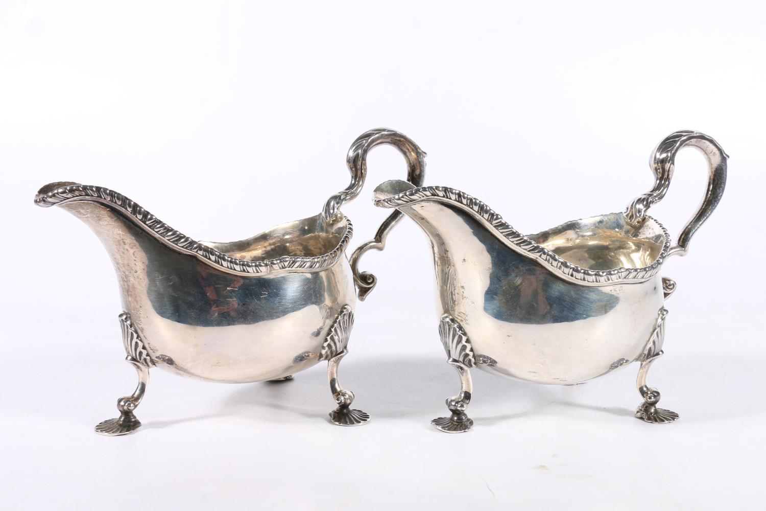 Pair of Georgian silver sauce boats with feathered edge and scroll handles raised on scallop shell