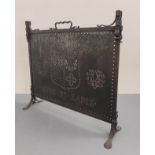 Dark metal firescreen with carrying handle and pierced panel with a coat of arms, on cheval