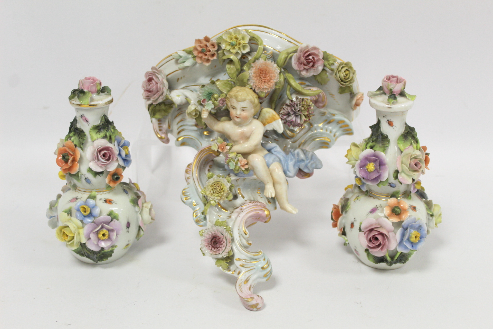 Sitzendorf porcelain wall bracket of rococo floral encrusted scroll form surmounted by a cherub with