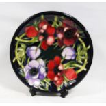 Modern Moorcroft plate decorated with tube lined red and violet anemones with green stalks on a blue