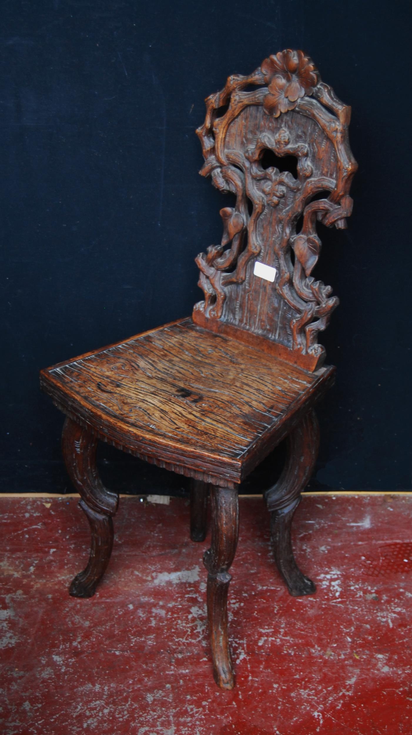 Black Forest carved oak hall chair, the naturalistic back rest applied with flowerheads and