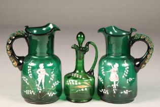 Trio of Mary Gregory painted emerald green glassware, consisting of two jugs and a decanter,