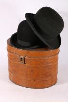 Two black bowler hats and a tin hat box.