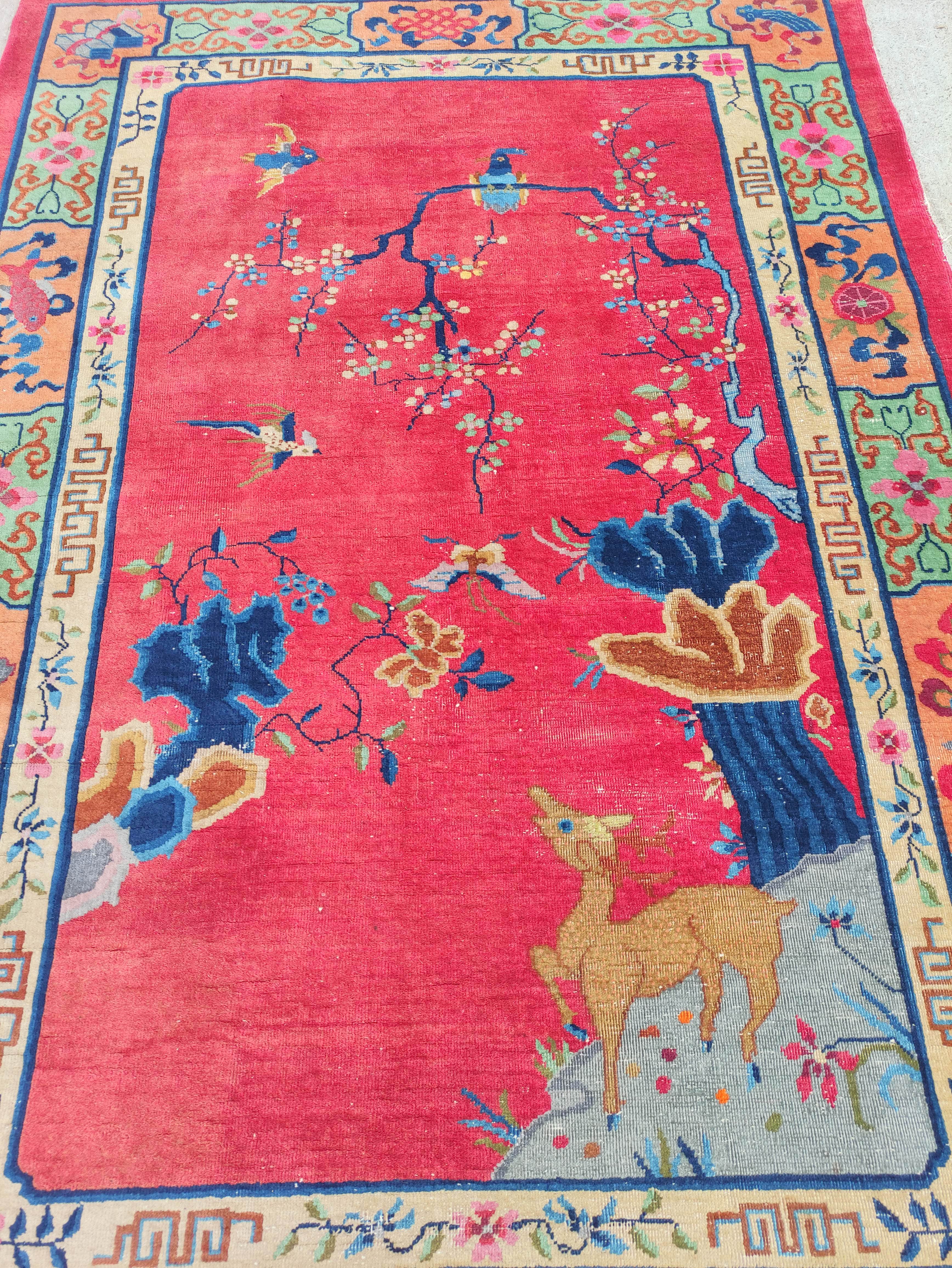 Chinese red ground rug, a deer in the corner below a blossom tree with birds, decorative cream guard - Image 2 of 4
