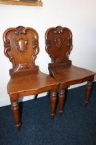 Pair of Victorian carved oak hall chairs, the shield backs with scroll border, raised on turned
