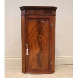 A George III and later mahogany corner cupboard, the hinged recessed panel door opening to reveal an