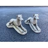 A pair of reconstituted stone garden ornaments, each modelled as a recumbent whippet upon an