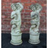 A pair of reconstituted stone cherubs, each modelled arm raised holding fruit, upon an integrated