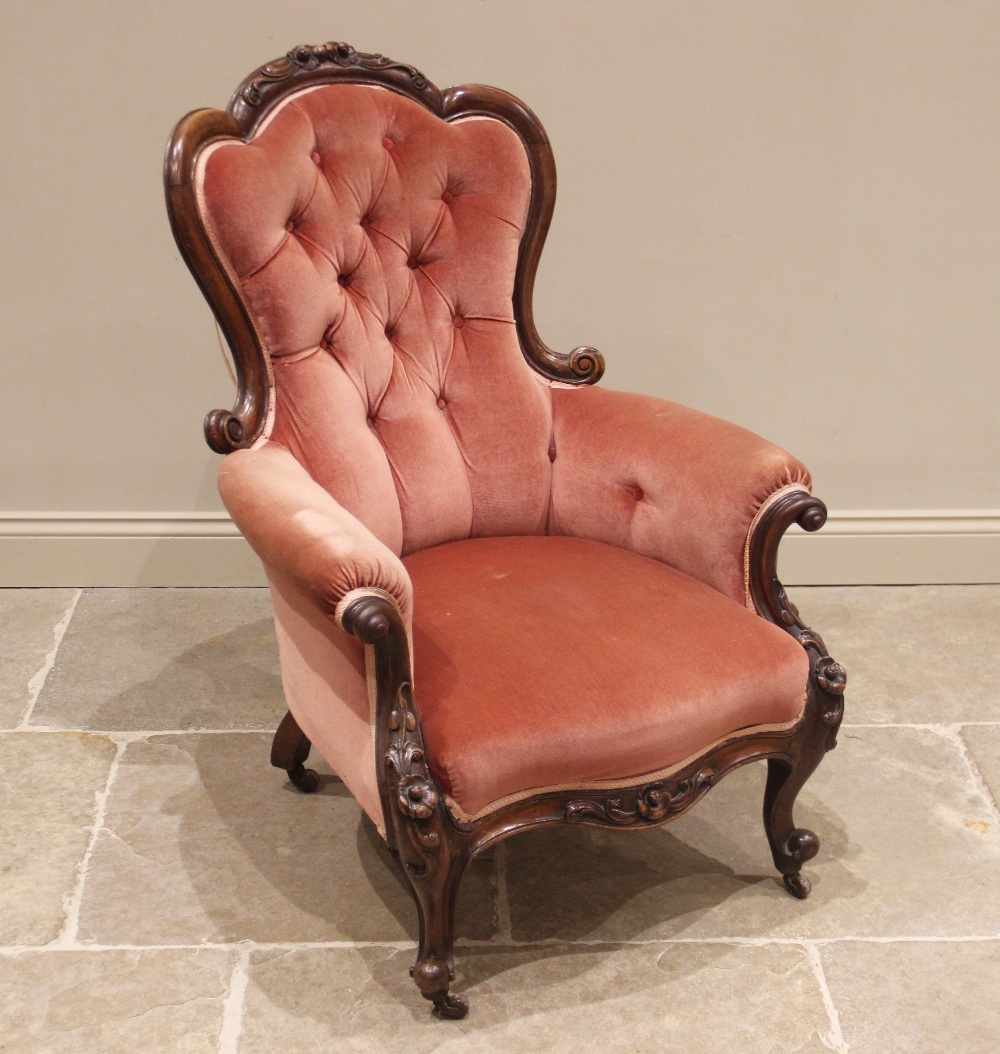 A Victorian carved walnut and rose pink velour salon chair, the shaped button back framed by a