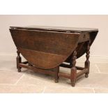 An 18th century oak drop leaf dining table, the oval plank top above a single frieze drawer, upon