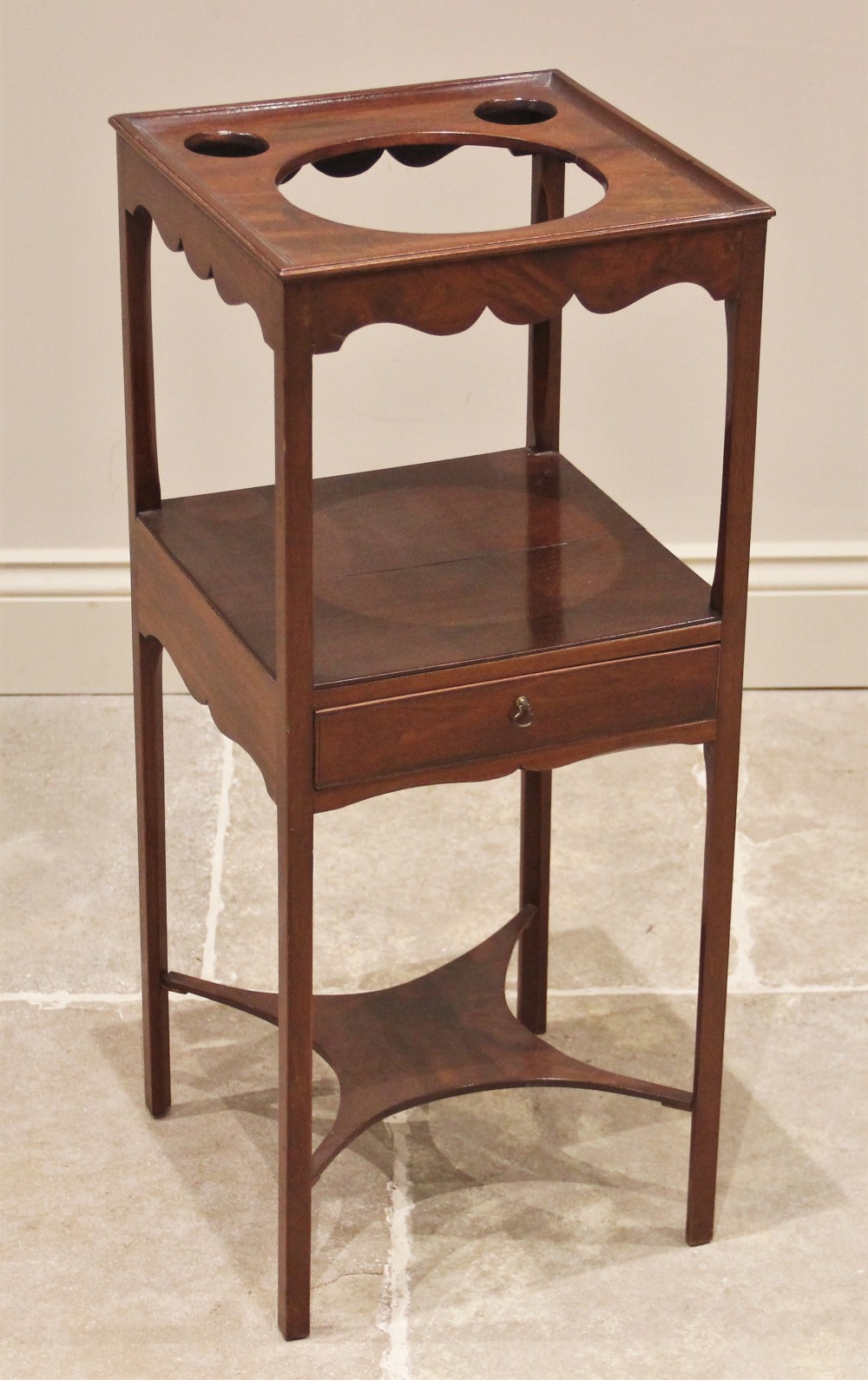 A George III mahogany washstand, the square top with a raised rim and three circular apertures, over