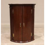 A George III oak bowfront hanging corner cupboard, the moulded cornice over a pair of convex doors