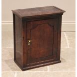 An 18th century oak spice cupboard, the moulded cornice above a single panelled door opening to